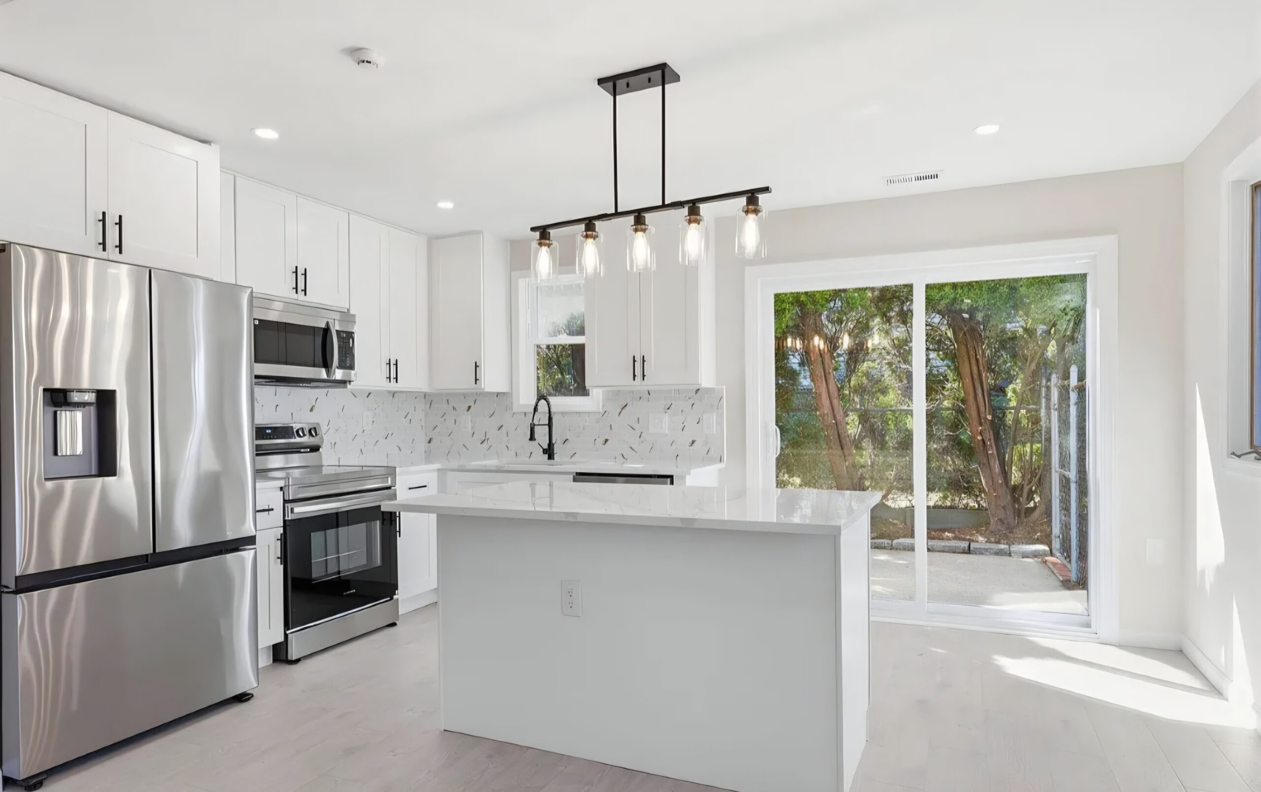White kitchen cabinets, island, pendant lights and sliding patio doors